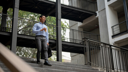 A confident Asian businessman walking down the stairs, holding a coffee cup and a briefcase.