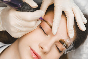 A cosmetologist applies permanent makeup to the eyebrows - eyebrow tattoo. eyebrow perm