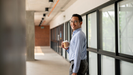 A confident Asian businessman walking along an indoor corridor, holding a coffee cup and a briefcase