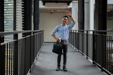 A friendly Asian businessman waving to greet his colleague while walking along the building corridor