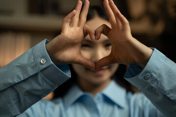 A woman of Asian descent demonstrates how to create a heart shape using her hands. She carefully...
