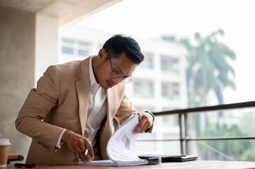 A determined Asian businessman searching for a document, concentrate on a document on a table.