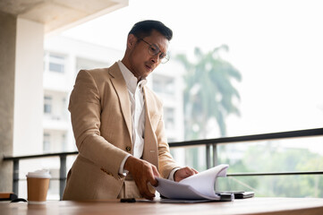A determined Asian businessman searching for a document, concentrate on a document on a table.