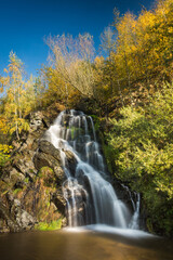 Fototapeta premium Early autumn colors on a sunny day at the 9 meter high waterfall in the village of Masty