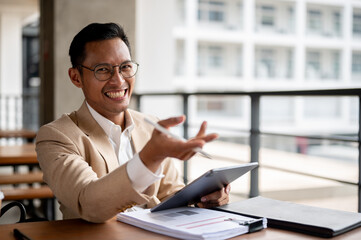 An enthusiastic Asian businessman smiles joyfully, gesturing with excitement while holding a tablet.