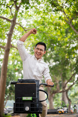 An excited Asian businessman rides a bike triumphantly, raising his fist in celebration.