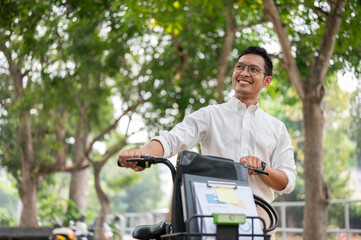 A happy, carefree Asian businessman pushing his bike, walking in the public park. - 781923260
