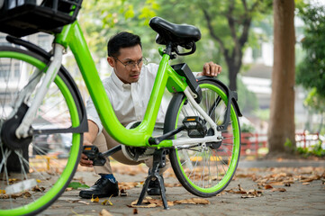 A focused businessman inspects his bicycle tire in a park, encountering an issue during his commute. - 781923425