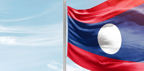 Laos national flag with mast at light blue sky.