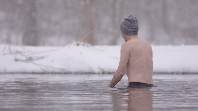 Funy shot of a novice ice bather plunging 3 times, in icy Nordic lakewater