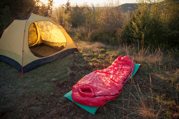 A yellow tent and a red sleeping bag in the forest at sunset
