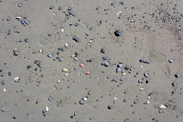 Stones, pebbles and shoe prints on beach sand texture