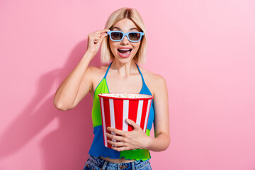Portrait of impressed woman with bob hairstyle wear colorful top touch 3d glasses hold popcorn at cinema isolated on pink color background