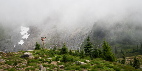 Man standing on top of rocks and raising arms high. Mt Rainier National Park in the fog. Washington State.
