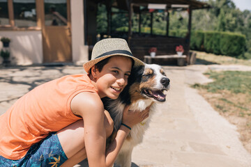 A girl while wearing a straw hat is hugging a dog