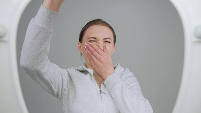 Woman opens toilet lid, looks through inside, grimaces at unpleasant smell, covers her nose with hand, shows disgust. View from toilet bottom. Cleanliness and hygiene concept