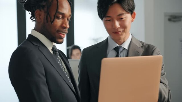オフィスでノートパソコンを見ながら会話する多国籍ビジネスパーソンのグループ