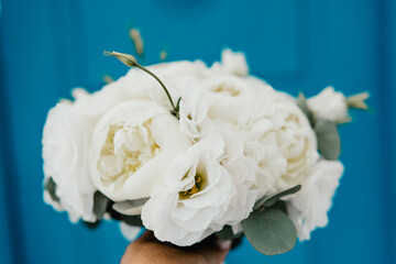 A bouquet of white flowers is being held by a person. The flowers are arranged in a vase and are placed on a blue background. The bouquet has a simple and elegant design.
