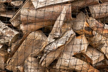 Closeup of a pile of cut firewood behind a mesh metal fence