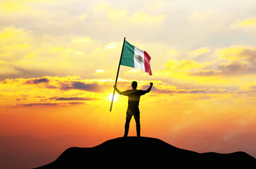Mexico flag being waved by a man celebrating success at the top of a mountain against sunset or sunrise. Mexico flag for Independence Day.