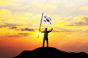 South Korea flag being waved by a man celebrating success at the top of a mountain against sunset...