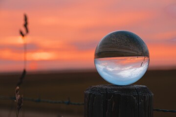 Glass ball on wooden pole against blur background in a field at sunset