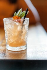 Vertical shot of a glass with an iced orange citrus cocktail and a straw on a wooden table