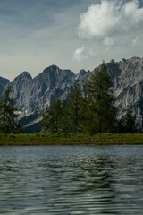 Vertical shot of a still lake in front of rocky mountains and evergreen trees
