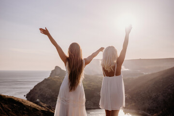 Two women are standing on a hill overlooking the ocean. They are holding hands and looking out at...