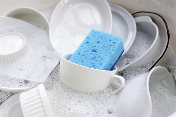 Dirty dishes with cleaning sponge in foam of dishwashing liquid. Washing dishes concept