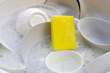 Dirty dishes with cleaning sponge in foam of dishwashing liquid. Washing dishes concept