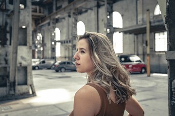 Rear of a female standing indoors in an empty building and sunlight in