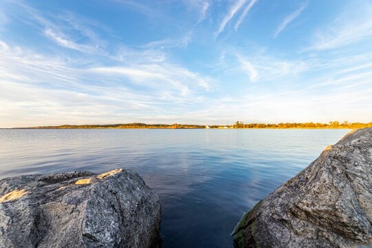 Scenic view of a rocky shore against a tranquil lake under a blue sky on a sunny day