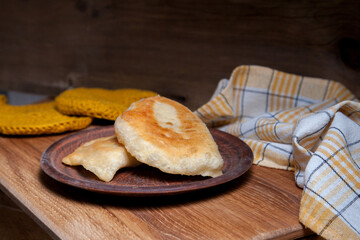 Clay plate of fried meat pies on wooden table.