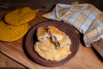 Clay plate of fried meat pies on wooden table.