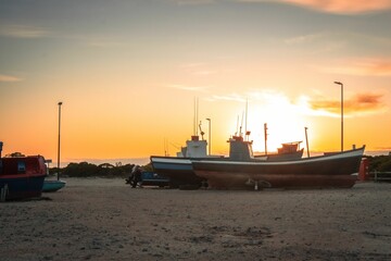Fototapeta premium Image of several boats on the water and beach under the sunset sky.