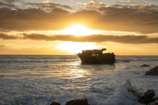 Image of a sing ship in the waves of the sea during the yellow sunset.