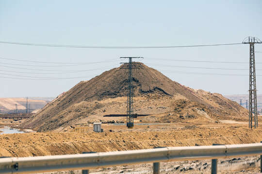 Large mound of earth near power lines under a clear sky in a desert environment. A vast mounds against the backdrop of a desert landscape, with electric power lines crossing in the foreground, Israel
