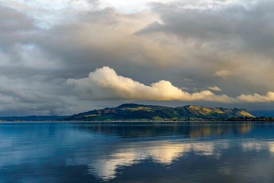 Picturesque view of Rotorua lake with a reflection of beautiful hills and fluffy clouds, New Zealand