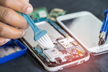 Asian technician repair and cleaning dirty micro circuit main board of smartphone electronic...