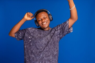 Happy Nigerian man listening to music on his headphone isolated on a blue background
