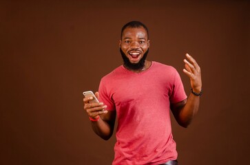 African man holding his phone and standing in front of a brown background