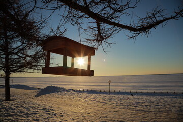 Hanging wooden gazebo in a snowy field during sunset