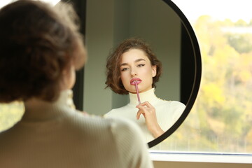 young woman looking in a mirror applying make up - 781991054