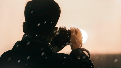 Closeup of a man holding a camera and taking a photo of the sun at sunset, surrounded by snowflakes