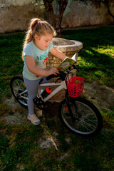 Niña caucásica pequeña con el pelo rubio leyendo un libro sentada en una piedra junto a una bici...