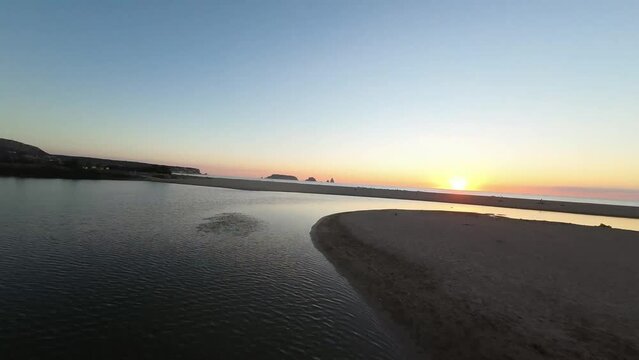 Drone shot over a scenic seascape and its sandy beach with a glowing sun at sunset in swift motion