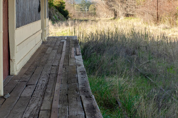 The aged wooden planks of Gundagai's abandoned train platform, overgrown grass weed over the rail tracks. The heritage-listed railway station is in New South Wales, Australia.