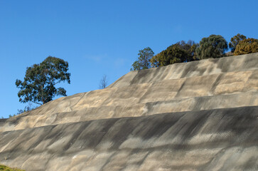 A tall concrete retaining wall or mechanically stabilized earth MSE wall, used alongside highways and in steep terrain to prevent soil erosion and landslides.