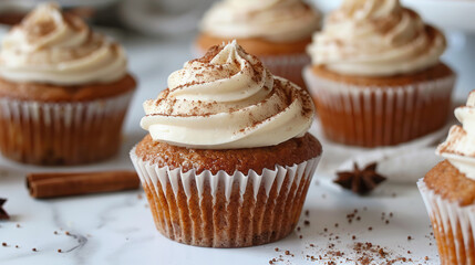 Cupcakes on a white table topped with cream cheese frosting and dusted with cinnamon